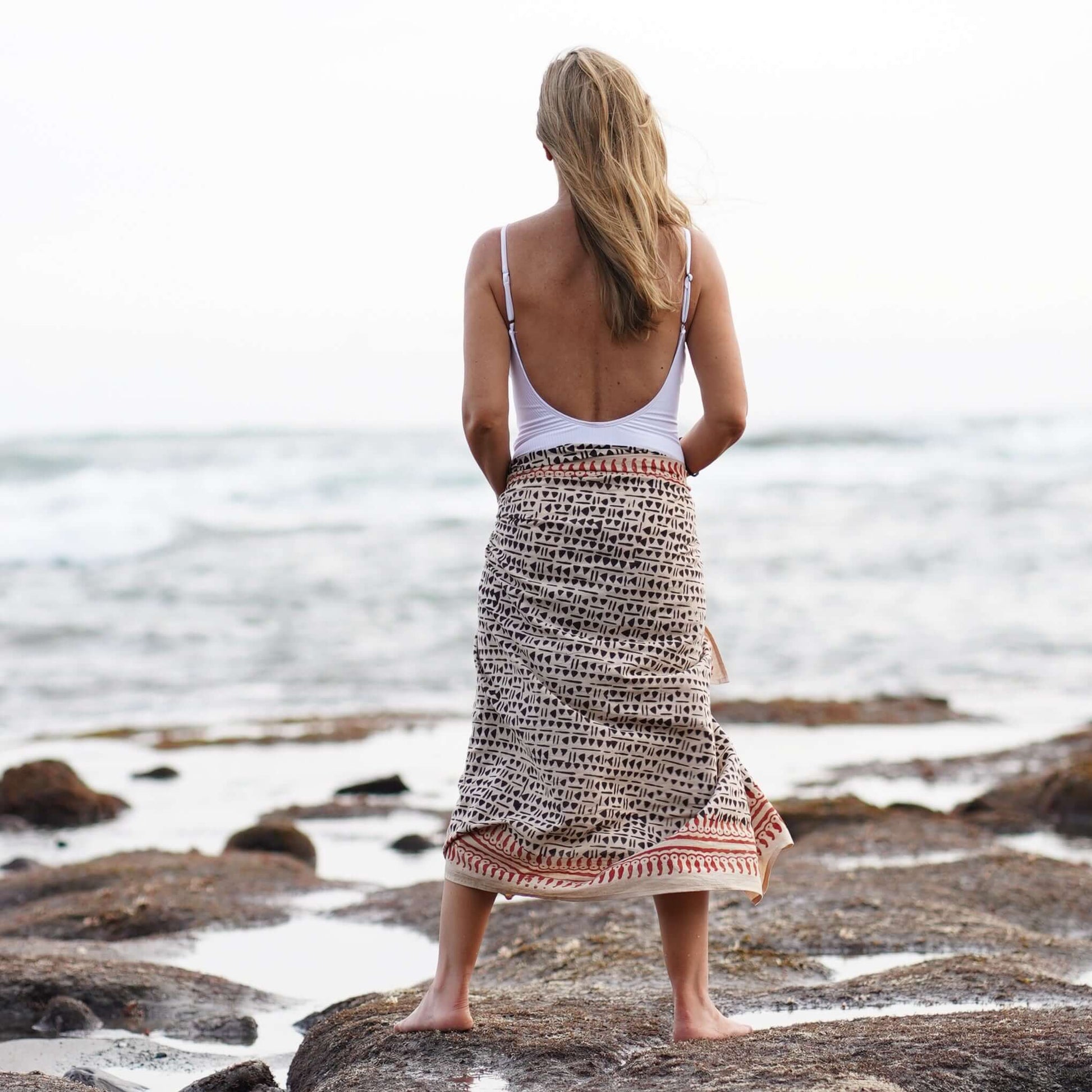 Women’s batik cotton sarong in black and brown pattern, tied at waist, beach setting, back view