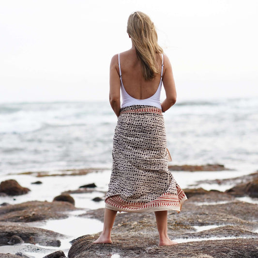 Women’s batik cotton sarong in black and brown pattern, tied at waist, beach setting, back view
