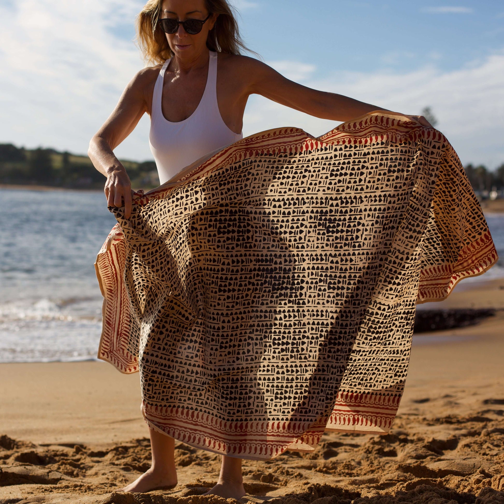 Women’s batik cotton sarong in black and brown pattern, tied at waist, beach setting, side view