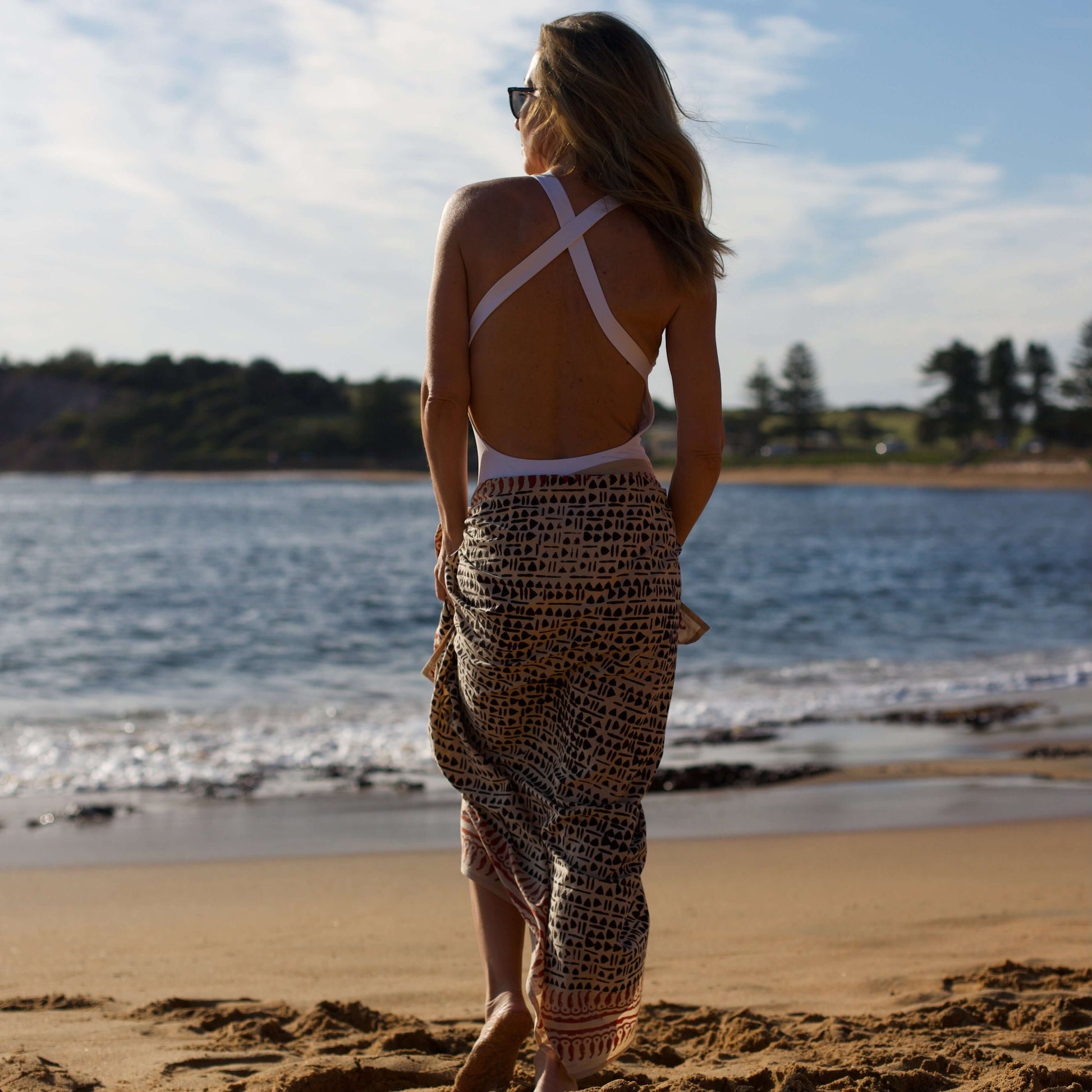 Women’s batik cotton sarong in black and brown pattern, tied at waist, beach setting, rear view