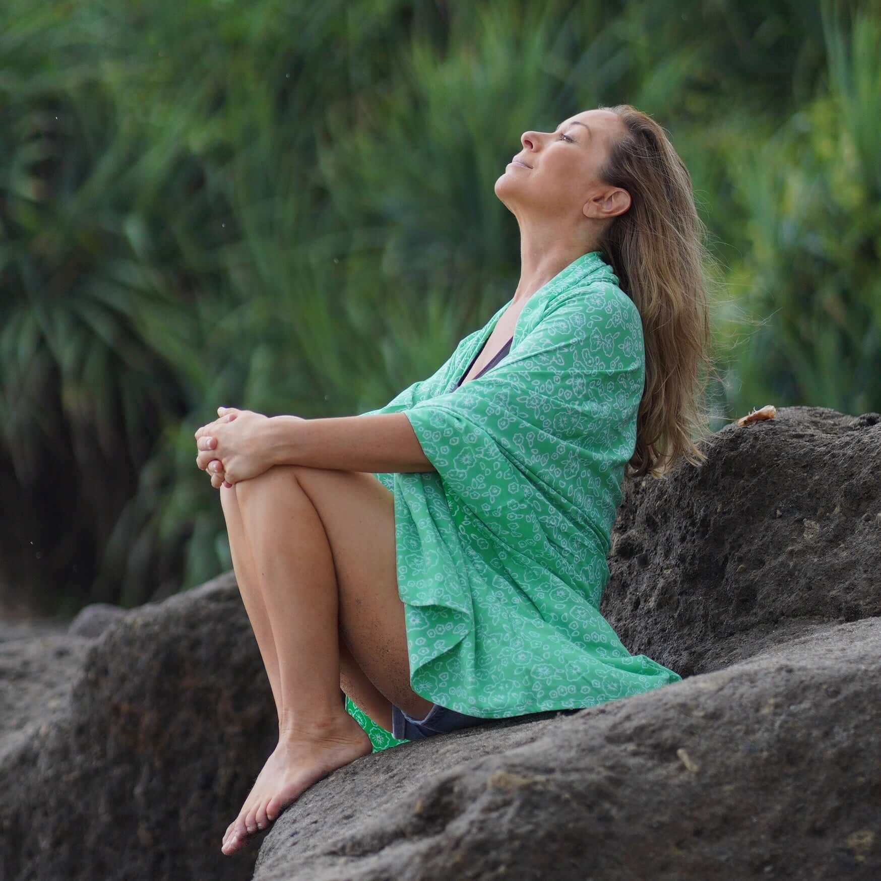 beautiful woman sitting in a rock in Bali wearing green beachcover-up