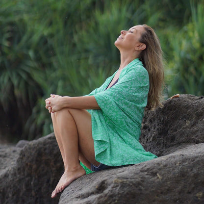 beautiful woman sitting in a rock in Bali wearing green beachcover-up