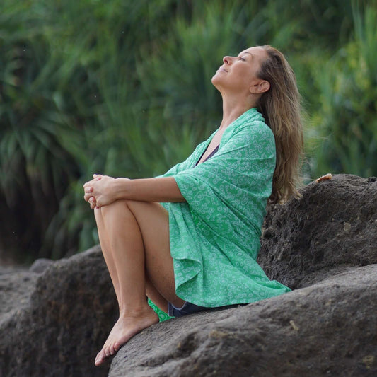 beautiful woman sitting in a rock in Bali wearing green beachcover-up